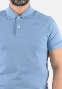 Polo di colore azzurro chiaro realizzato in misto cotone, con colletto, tre bottoni e un logo ricamato discreto sul petto.