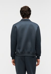 Sudadera azul oscuro con textura suave, dobladillo y puños acanalados. Cuenta con un cuello abierto y un diseño de ajuste relajado.