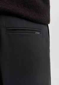 Czarne spodnie o gładkiej fakturze, z jedną tylną kieszenią i małą metką z logo "JACK & JONES."