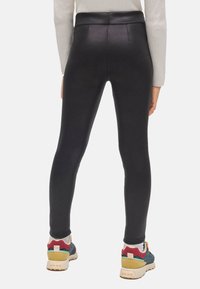 Leggings negros con una textura brillante, cinturilla alta y detalles cosidos, combinados con zapatillas deportivas multicolores con suela de goma.
