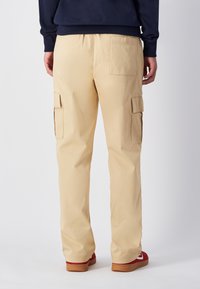 Pantaloni cargo beige con molteplici tasche laterali, vestibilità ampia e gambe dritte, abbinati a scarpe da ginnastica rosse e una maglia blu navy.