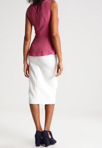 Atasan tanpa lengan yang pas di badan berwarna merah muda tua, dengan pinggang peplum, dipadukan dengan rok pensil putih yang panjangnya sampai lutut dan sepatu hak tinggi berwarna navy.