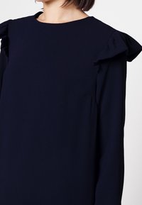 Námořnické šaty s dlouhým rukávem, které mají volánkové detaily na ramenou a kulatý výstřih, vyrobené z hladké, lehké látky.