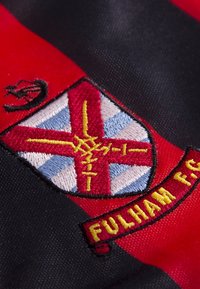 Rood en zwart stof met geborduurd Fulham FC-embleem, featuring een rood en blauw schild, gele accenten en witte details.
