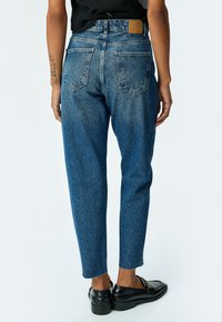 Pantalones de mezclilla de color azul claro con un corte relajado, que cuentan con cinco bolsillos, dobladillos de tobillo deshilachados y un parche de cuero marrón en la parte trasera de la cintura.