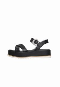 Sandalias de plataforma negras hechas de cuero suave, con tiras entrelazadas y una hebilla metálica. La suela blanca con borde serrado proporciona tracción.