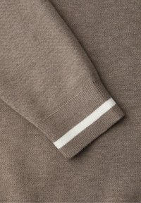 Manche de pull en tricot taupe avec un poignet côtelé présentant une seule bande blanche près du poignet.