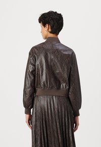 Chaqueta bomber marrón con textura de piel de serpiente, puños y dobladillo acanalados, material brillante y una silueta ajustada.