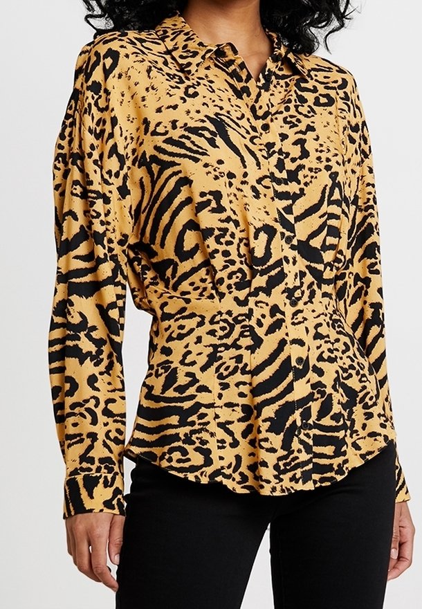 Chemise boutonnée en tissu jaune avec un motif animalier noir. Manches longues et col avec une coupe ajustée.