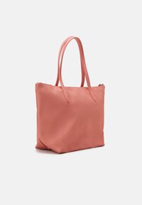 Rosa tote-väska med en slät yta, dragkedjestängning och två handtag. Rektangulär form med något rundade hörn och en platt botten.