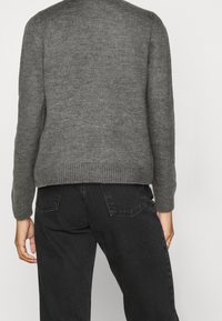 Maglione grigio a maglia con scollo rotondo e orlo a costine, abbinato a jeans scuri con tasche posteriori e gamba dritta.