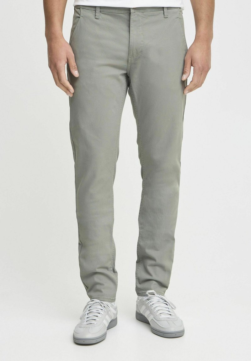 Lichtgrijze broek van katoenmix, met een slim fit ontwerp, zijzakken en een platte voorkant, gecombineerd met witte sneakers.