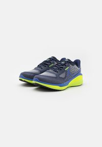 Chaussures de course pour hommes avec un dessus en maille bleu marine et des accents gris, semelle jaune vif, détails bleus et grip texturé.