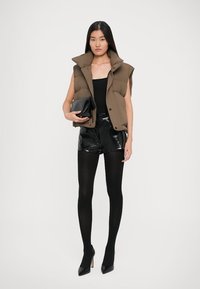 Brunærmeløs puffer vest, sort tætsiddende top, skinnende sorte shorts og sorte strømpebukser, suppleret med sorte stiletter og clutch-taske.