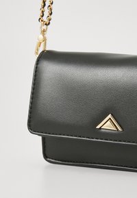 Black leather bag with a flap closure, gold hardware, and a triangular accent. Features a textured surface and a chain strap.