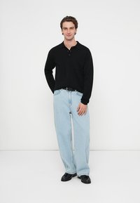 Musta pitkähihainen poolopaita, jossa on kaulus ja napit edessä, yhdistetty vaaleansinisiin leveälahkeisiin farkkuihin ja mustiin kenkiin. Yksinkertainen malli ja istuvuus.