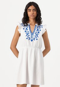 Λευκό βαμβακερό φόρεμα με μπλε λουλουδάτο κέντημα, διακοσμημένο λαιμό και ριχτές κάπες. Έχει ελαστική μέση και τσέπες.