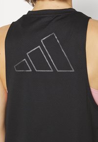 Top deportivo negro sin mangas que presenta una tela texturizada y un logo reflectante de tres franjas en la parte posterior.