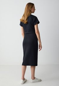 Abito nero aderente con maniche corte e lunghezza midi. Tessuto liscio, caratterizzato da un design semplice. Abbinato a sneakers bianche.
