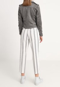 Gray faux suede motorcycle jacket with epaulets, paired with white and black striped wide-leg pants. White footwear completes the look.