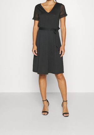 Schwarzes Kleid mit V-Ausschnitt, kurzen durchsichtigen Ärmeln und einem Bindegürtel in der Taille. Mittellange Ausführung mit einer glatten, leichten Textur.