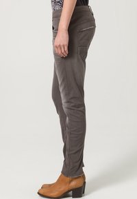 Grå slim-fit byxor i stretchdenim, med en medelhög midja, framfickor och subtila sömmar. Kombineras med bruna klackstövlar.