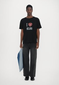 Black cotton t-shirt with "I ❤️ MILANO" print, paired with dark denim wide-leg pants and holding a two-tone denim jacket.