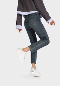 Jeans in denim blu scuro con taglio dritto, abbinati a sneaker bianche con un accento verde menta sul retro e tacco testurizzato.