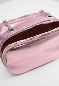 Borsa a tracolla metallica rosa con due compartimenti con zip, hardware argentato e una texture liscia. L'interno presenta un colore a contrasto.
