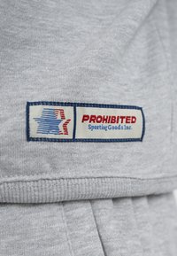 Étiquette de vêtement sur tissu gris avec un logo étoile bleu et rouge et texte indiquant "PROHIBITED Sporting Goods Inc."