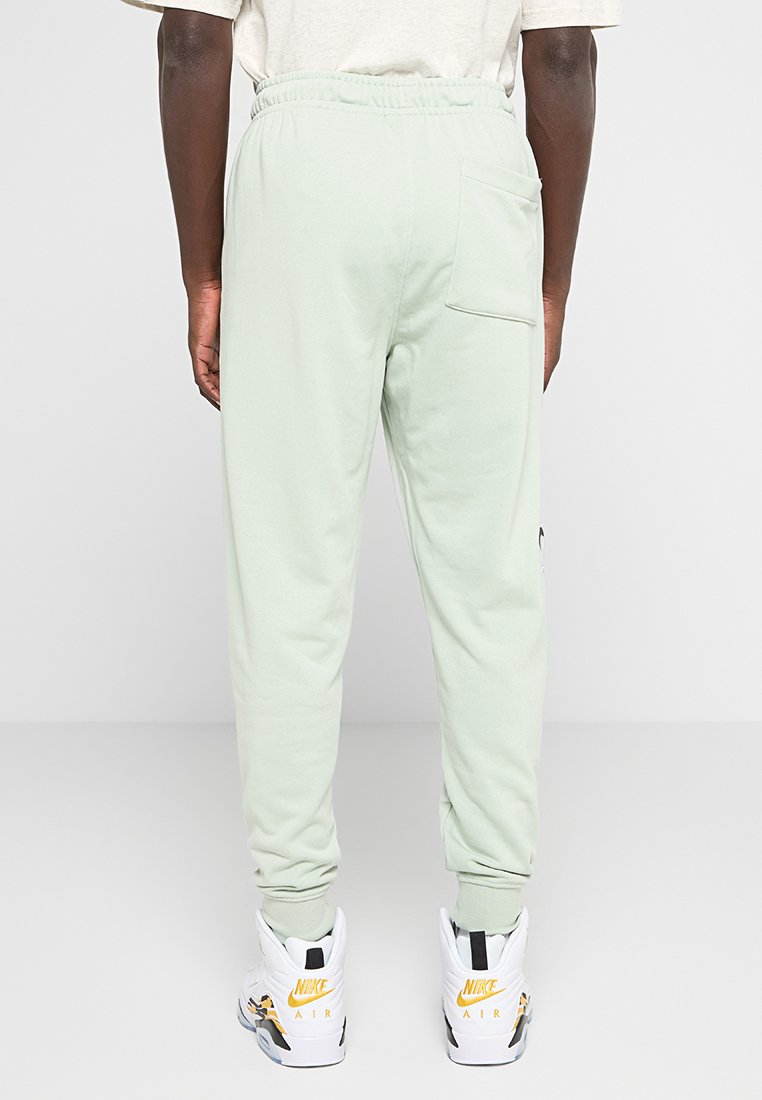 Pantaloni sportivi verde chiaro con vita elasticizzata, polsini a coste e una tasca posteriore. Indossati con scarpe da ginnastica bianche e gialle.