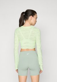Jasnozielony krótki top z długim rękawem z powtarzającym się wzorem "Nike Pro", w połączeniu z jasnzielonymi szortami z wysokim stanem z małym białym logo.