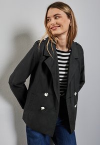 Chaqueta negra de doble botonadura con botones brillantes, con cuello con muescas y un ajuste relajado, sobre una camiseta de rayas en blanco y negro.