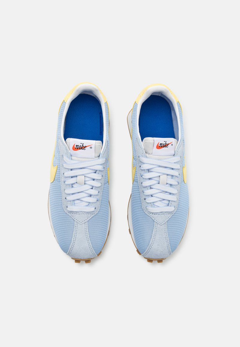 Zapatillas deportivas de malla azul y ante, con cordones blancos, detalles amarillos y una plantilla azul. Suela de goma con patrón de tachuelas para mayor tracción.
