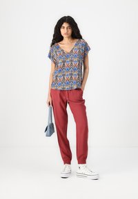 Blue and cream patterned short-sleeve top with a v-neck; red drawstring pants; white sneakers; small blue handbag.