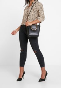 Black faux leather handbag with a gold-tone circular handle, paired with a leopard print blouse and ripped black skinny jeans.