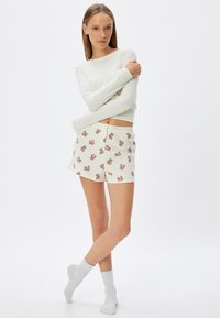 Lettet, cremegul langærmet top parret med mønstrede shorts med teddy-bjørn motiver. Begge dele er bløde, afslappede og komfortable.