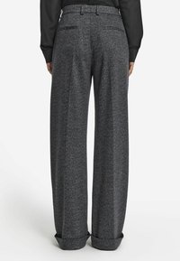 Person som bär grå herringbone ullbyxor med hög midja, vida ben och uppvikta fållar, tillsammans med en svart långärmad topp.