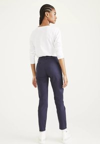 Granatowe spodnie slim fit z gładkiego materiału, tylnymi kieszeniami i średnim stanem, zestawione z białą koszulą z długim rękawem.
