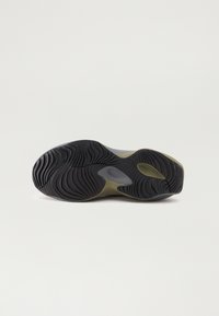Semelle d'une basket avec un motif de semelle ondulé noir et des accents beige, présentée isolément sur un fond clair uni.