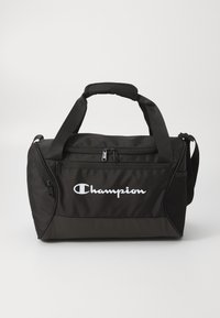 Svart stoff duffelbag med skulderrem, som har en glidelåslukking, meshlomme på siden og en fremtredende hvit "Champion"-logo på forsiden.