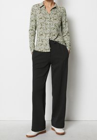 Camicia a maniche lunghe verde a stampa con design a bottoni e pantaloni neri a gamba larga. Completa l'outfit un paio di scarpe bianche con suola marrone chiaro.