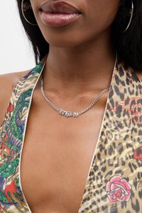 Colar de corrente prateada com a palavra "fantasia" em uma fonte cursiva, usado sobre um top halter estampado colorido.