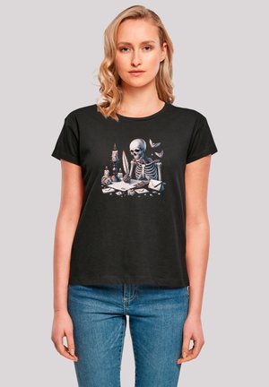 Schwarzes Baumwoll-T-Shirt mit einer Skelett-Illustration, das an einem Schreibtisch mit Kerzen und Umschlägen schreibt, rundem Hals und kurzen Ärmeln.
