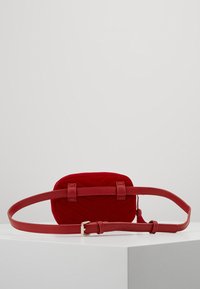 Czerwona pikowana torba na ramię z miękkiego materiału, wyposażona w gładki skórzany pasek i złote okucia, o prostokątnym kształcie.