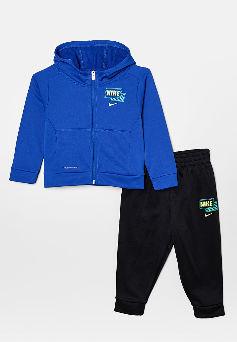 Felpa blu con zip e logo, abbinata a pantaloni jogger neri con logo in accenti verdi e gialli. Tessuto morbido e sportivo.