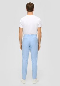 Hellblaue Hose aus glattem, strukturiertem Stoff mit Gesäßtaschen und taillierter Passform, kombiniert mit einem schlichten weißen T-Shirt.