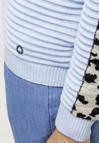 Pull en maille côtelée bleu clair avec un panneau texturé ornée d'un accent en imprimé animal noir et beige, terminé par un petit détail de logo.