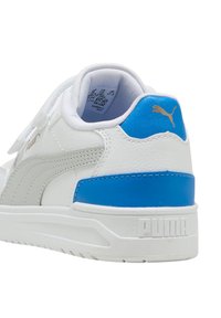 Zapatilla blanca con acento azul, parte superior de cuero, cuello acolchado y suela blanca texturizada. Presenta una marca dorada y un diseño de franjas laterales.