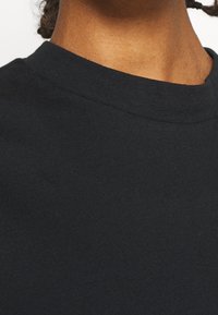 Camiseta negra de algodón de cuello redondo con una textura suave y un diseño simple y sin adornos. La tela parece blanda y transpirable.